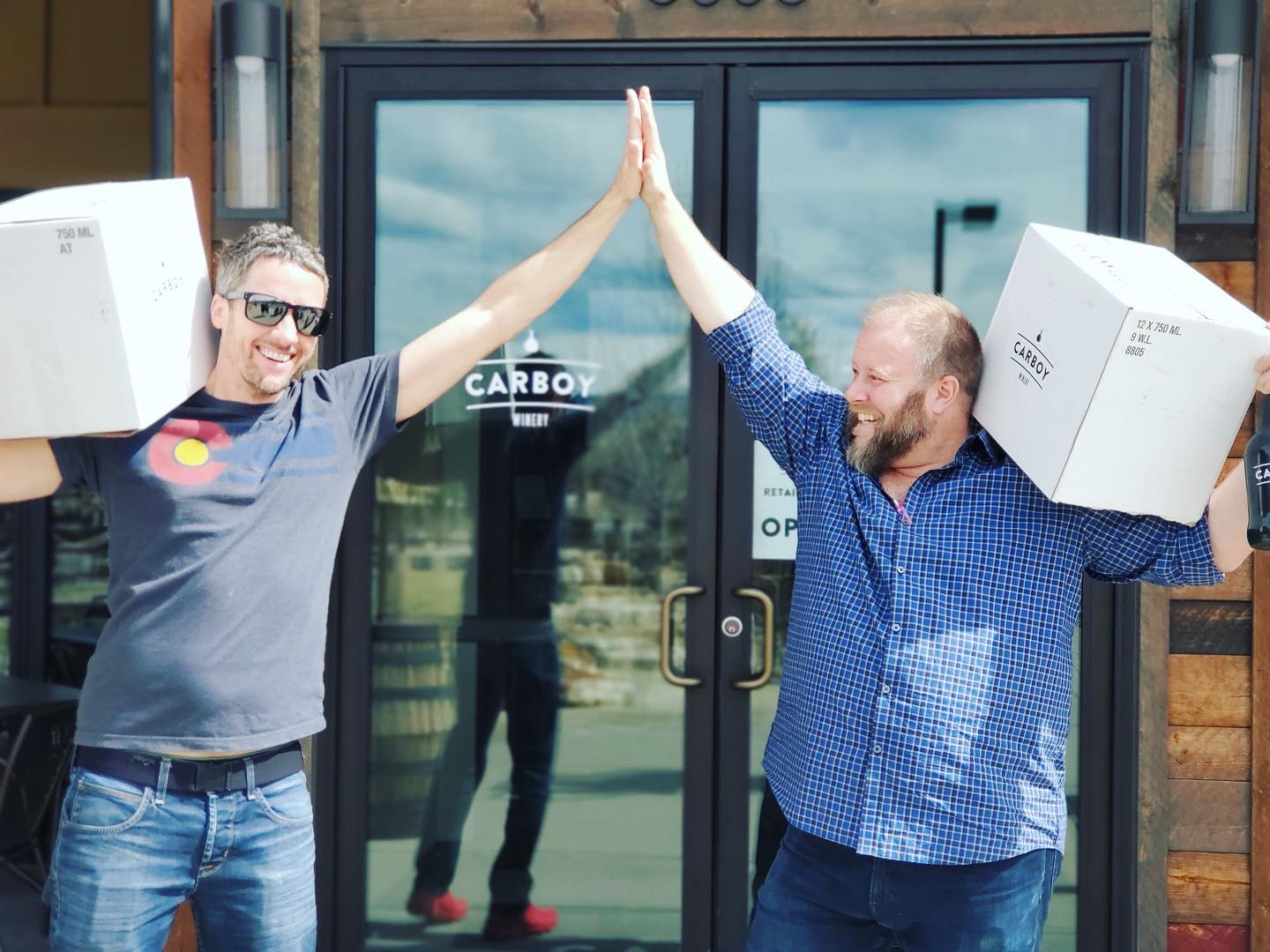 Image of two people with wine cases on their shoulders at Carboy Winery in Denver, Colorado