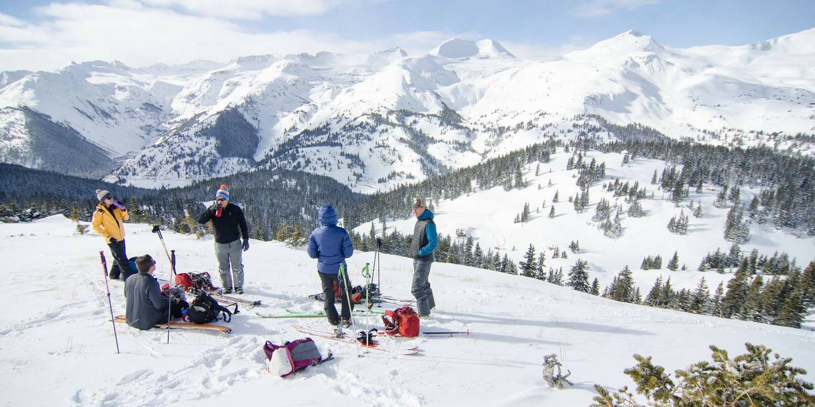 Image of skiers and snowboarders enjoying a drink at the top of Bluebird Backcountry in Colorado