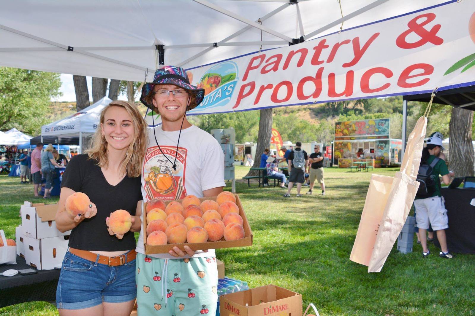 Image of two people at a produce stand holding peaches a the Palisade Peach Festival in Colorado