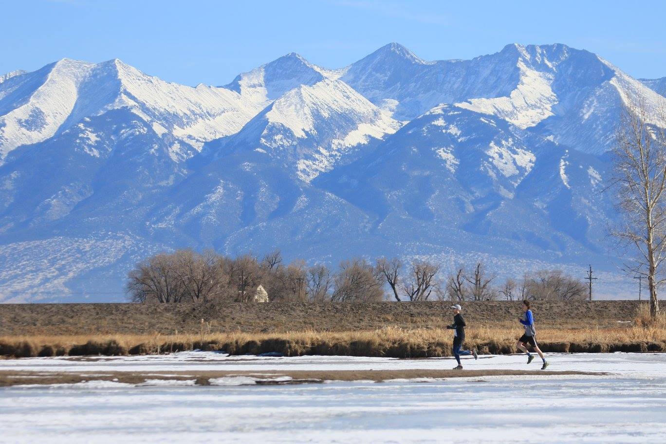 Two runners on a frozen river in front of mountain range