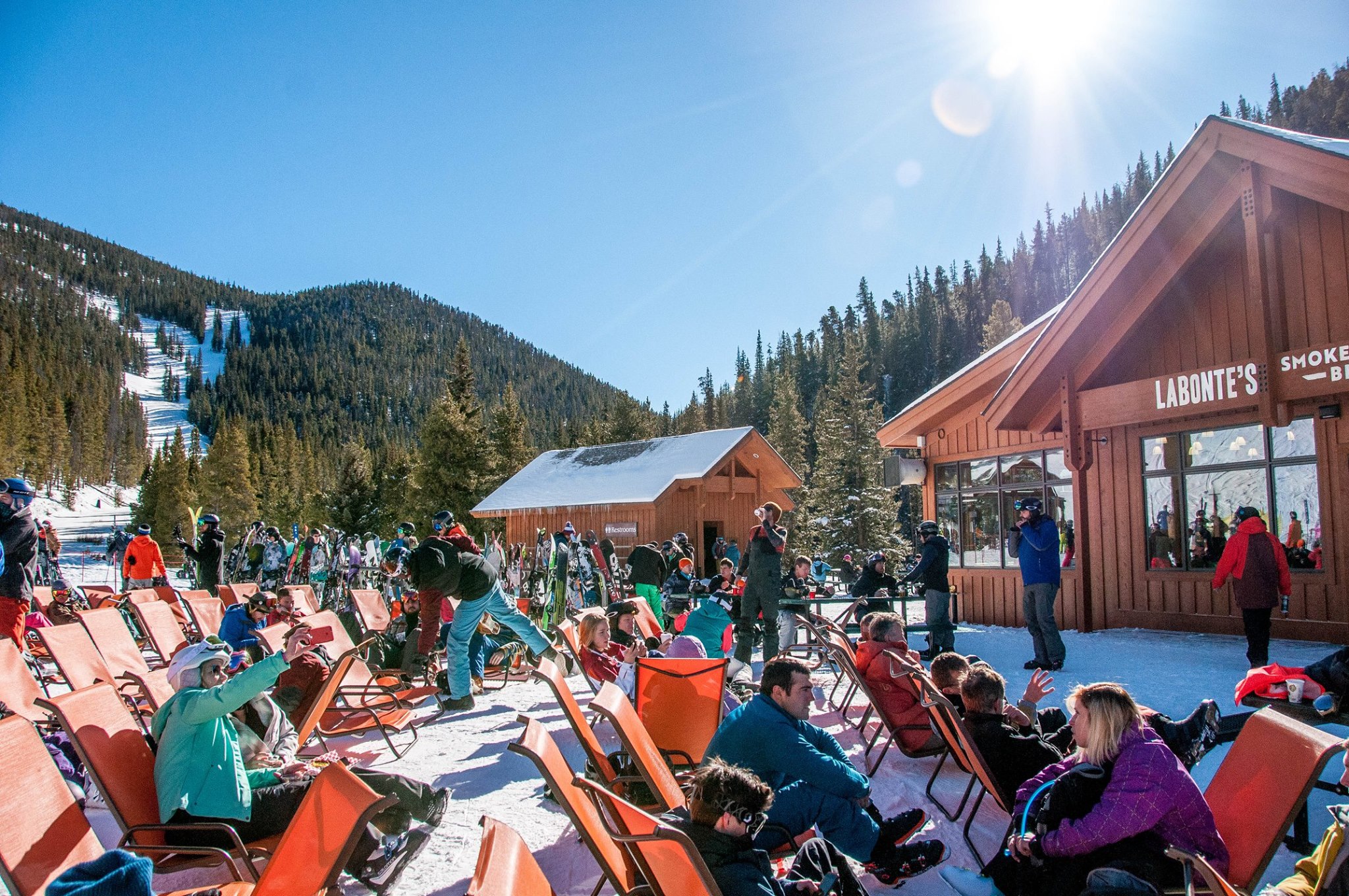 Skiers and snowboarders sitting outside of Labonte's Smokehouse in orange chairs on a sunny day