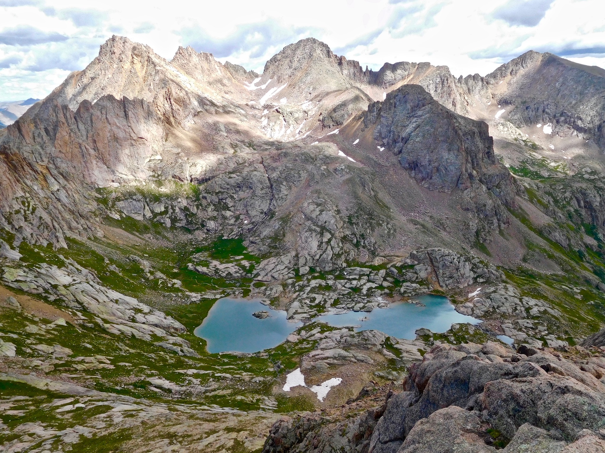 High alpine area of the San Juan Mountains with crystal clear lakes, green slopes, rocky cliffs and summit pinnacles.