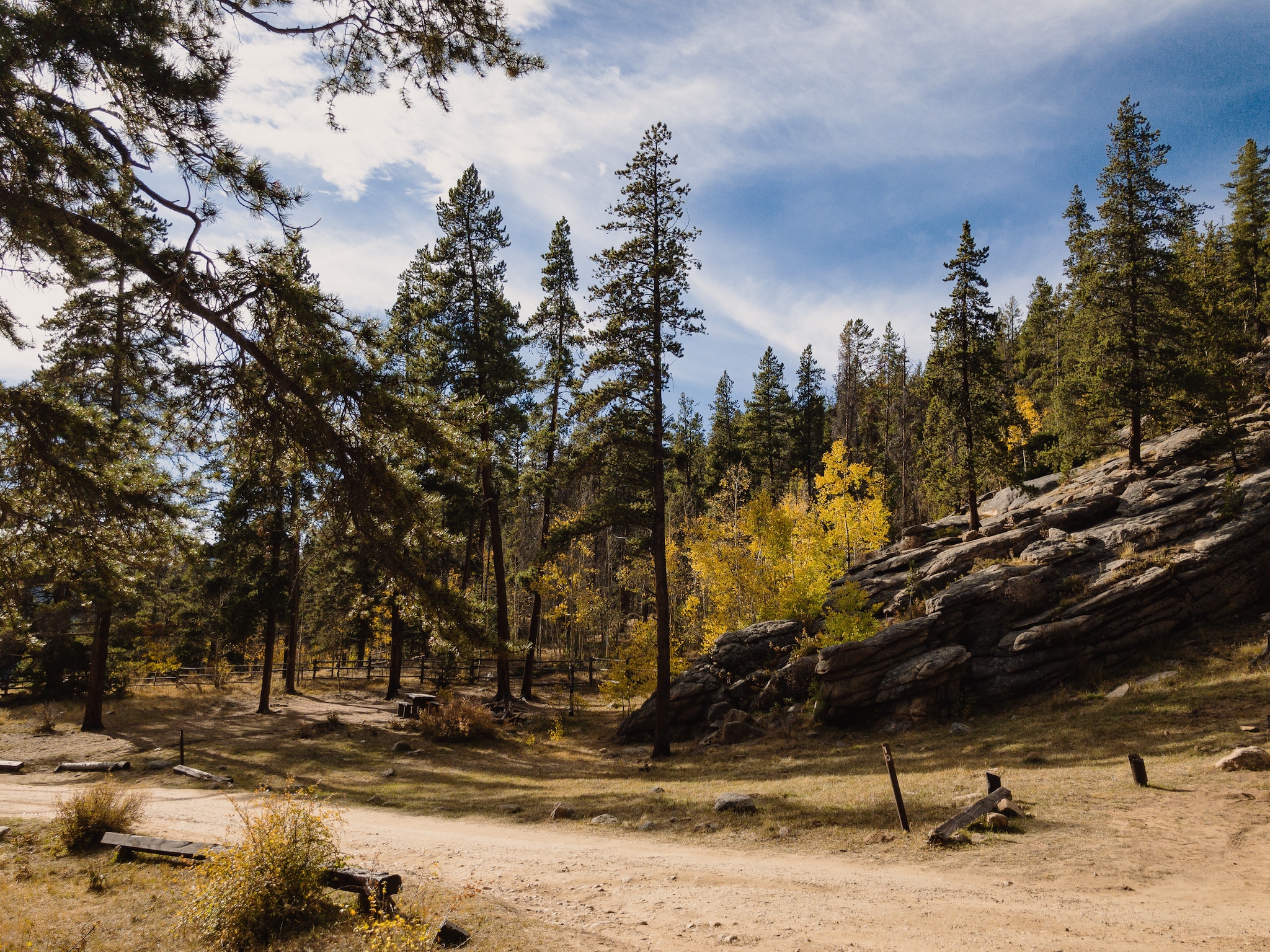 A mountain campground with car access, sparse trees, and slanted rocks.