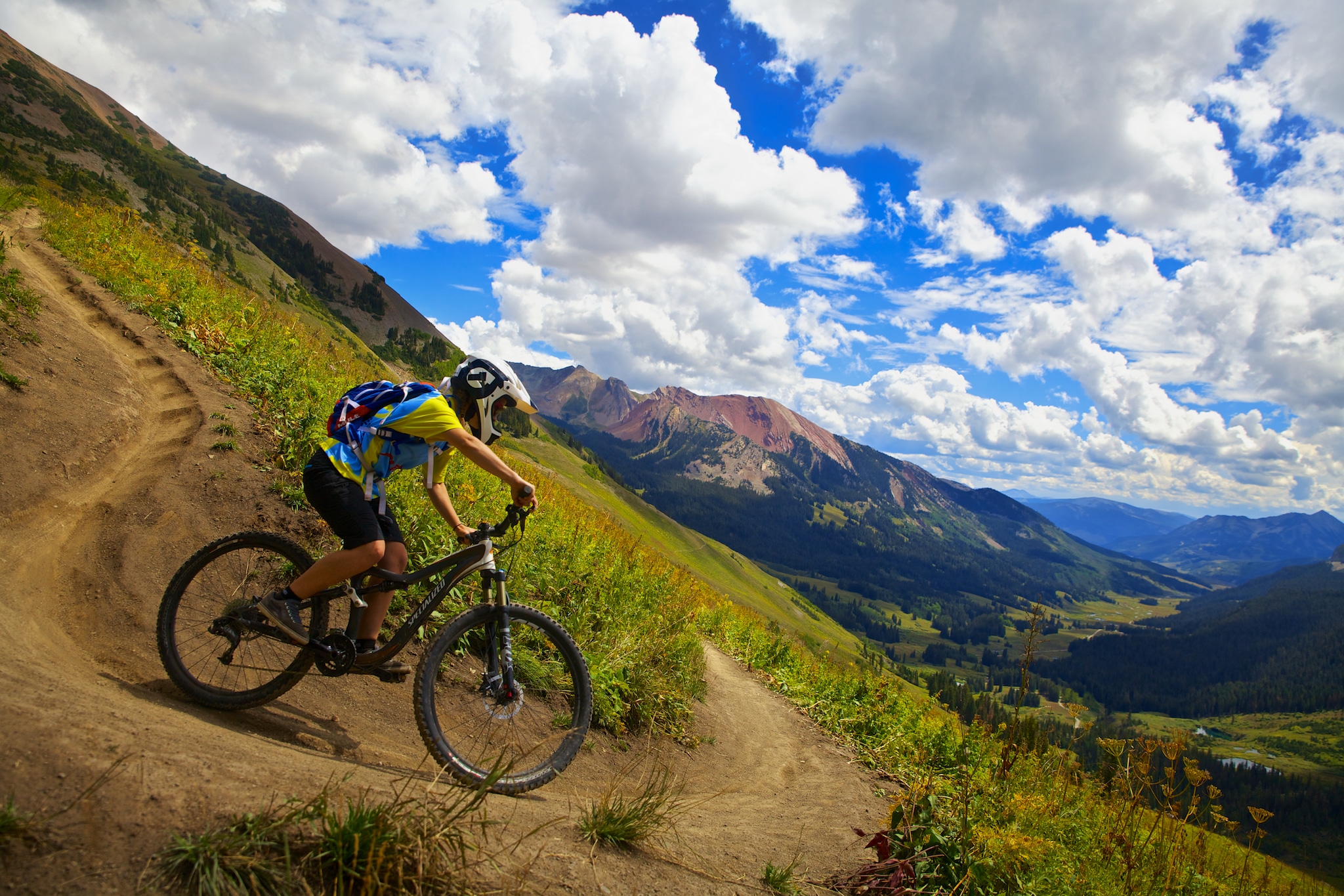 A tight switchback above treeline on the 401 bike trail with mountains and green valleys behind.