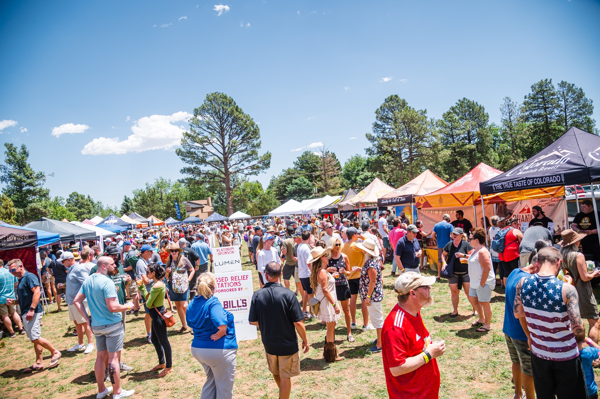 Sunny day with crowd of people mingling on the lawn at the Feast of Saint Arnolds. There are multiple brewery tents lining the perimeter.