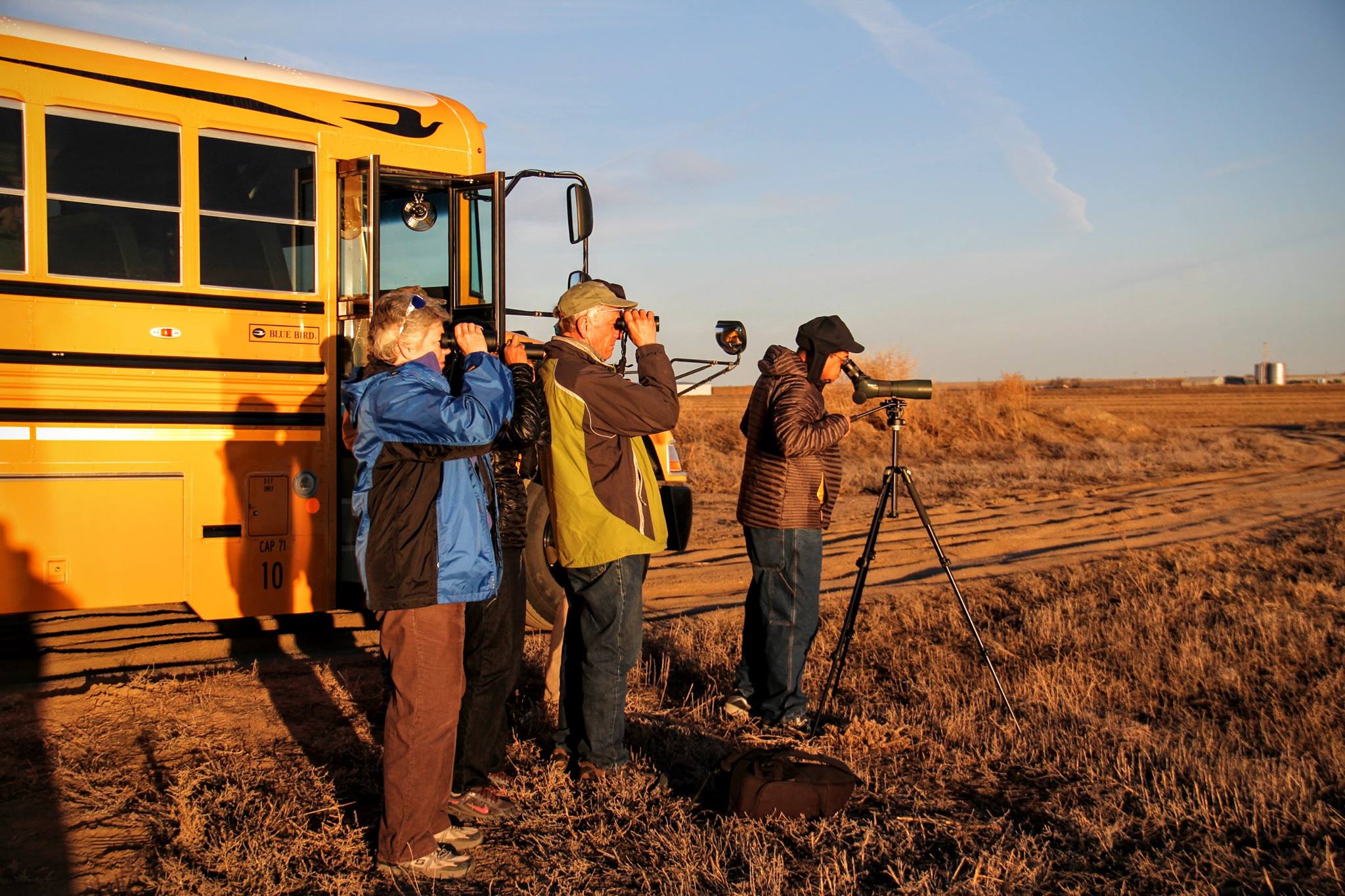 3 people with binoculars in front of a schoolbus