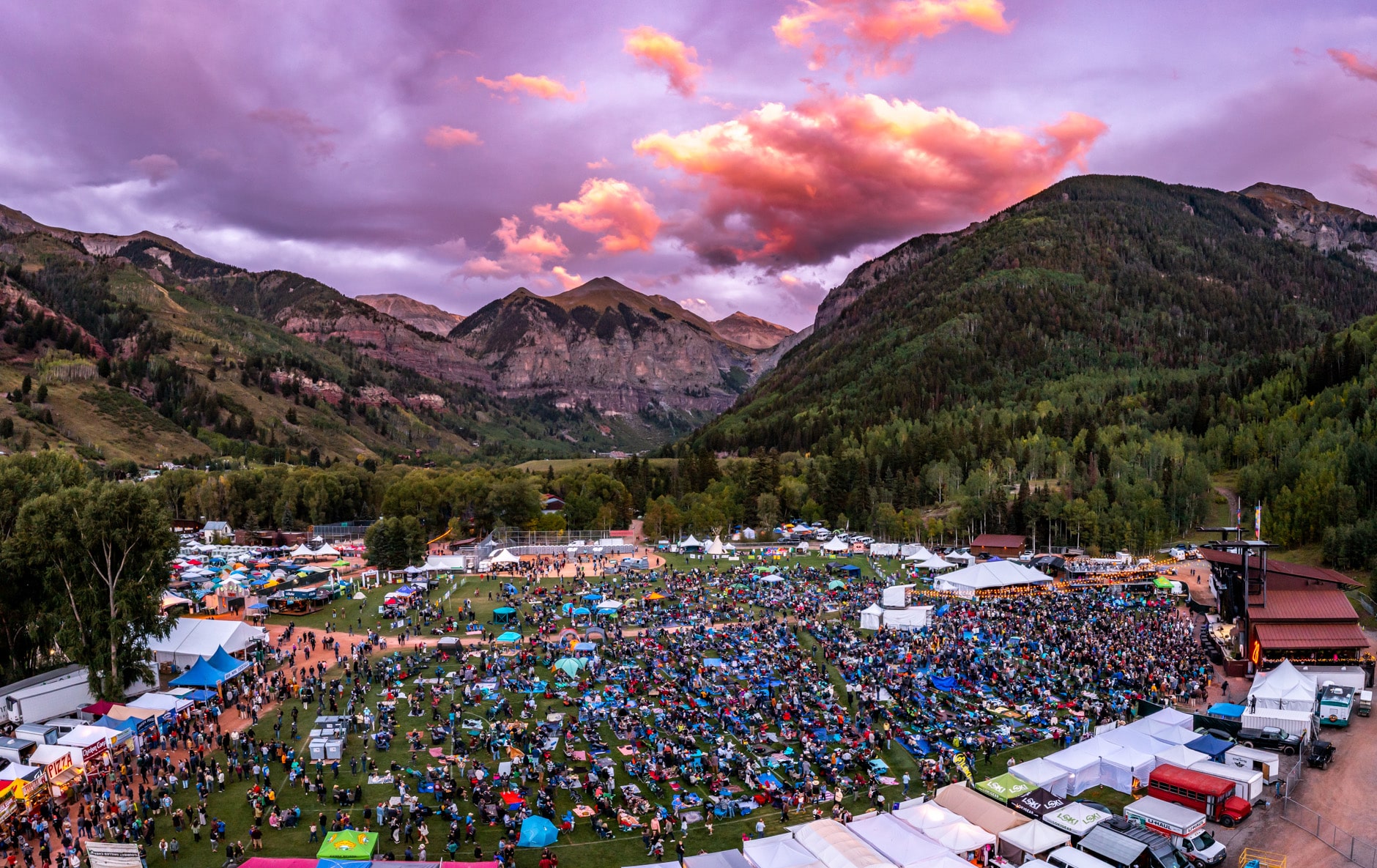 Kerumunan besar orang di Telluride Blues & Brews Festival dikelilingi oleh tenda penjual kanvas dan pegunungan hijau