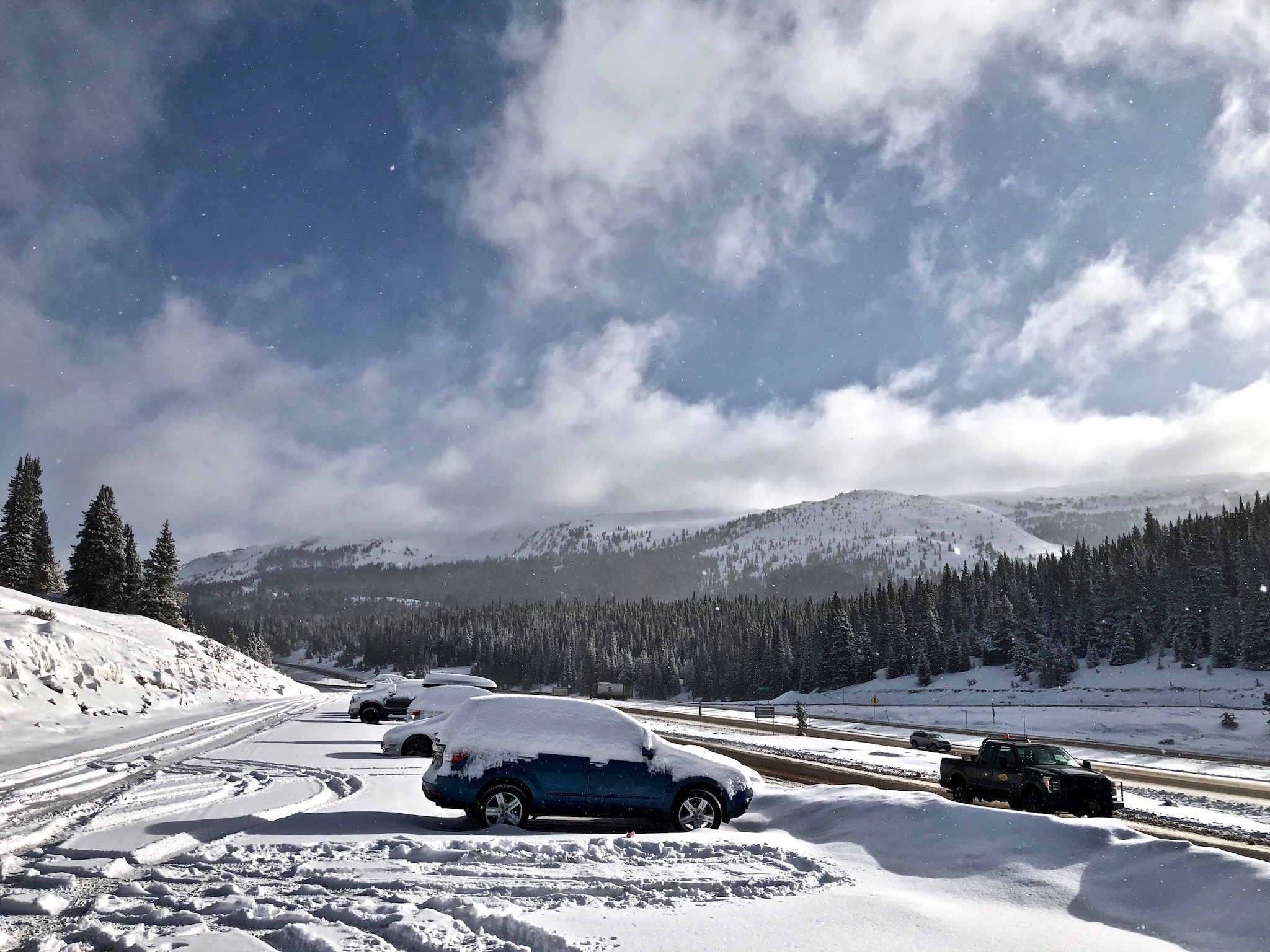 Patchy clouds, deep blue skies, and snow-covered cars along the crest of Vail Pass.