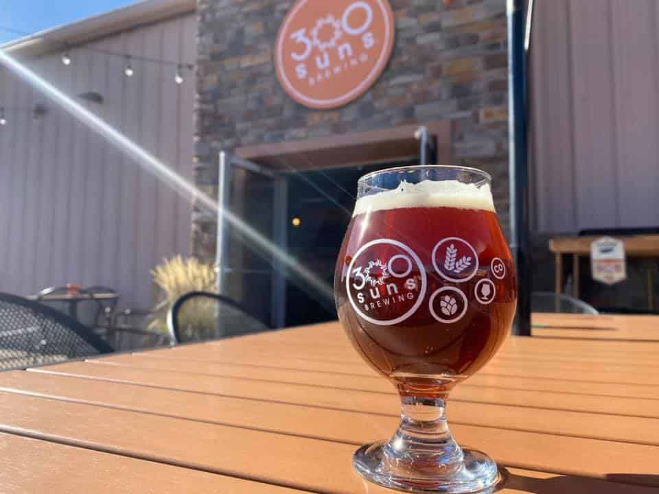 Glass of beer in front of 300 Suns Brewing entrance