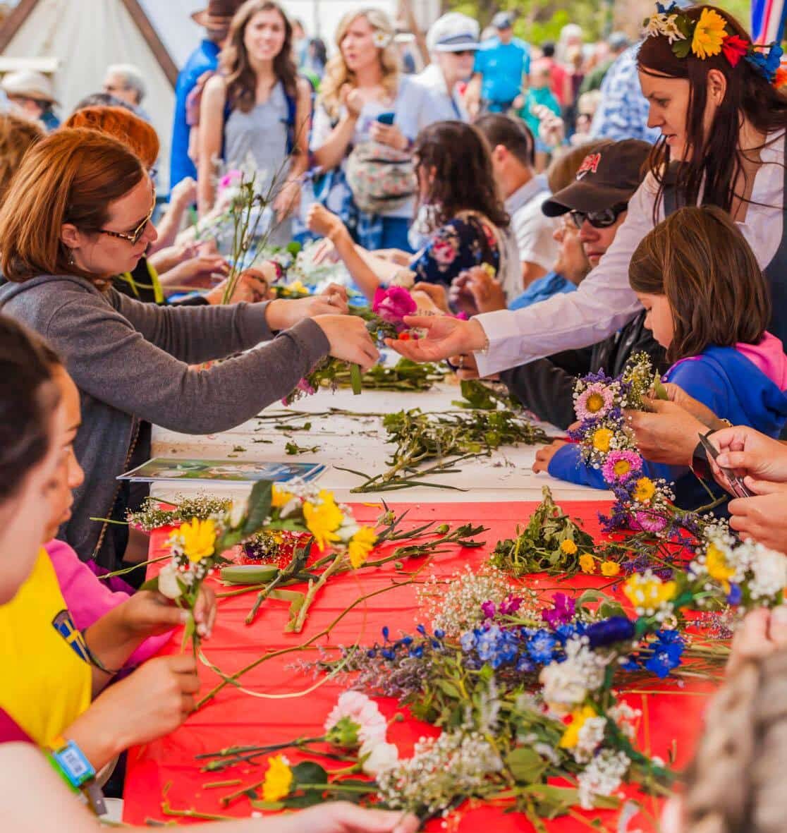 Long table covered in loose flowers with people on either side grabbing them to make flower crowns