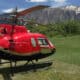 Red helicopter in field with mountains in the back