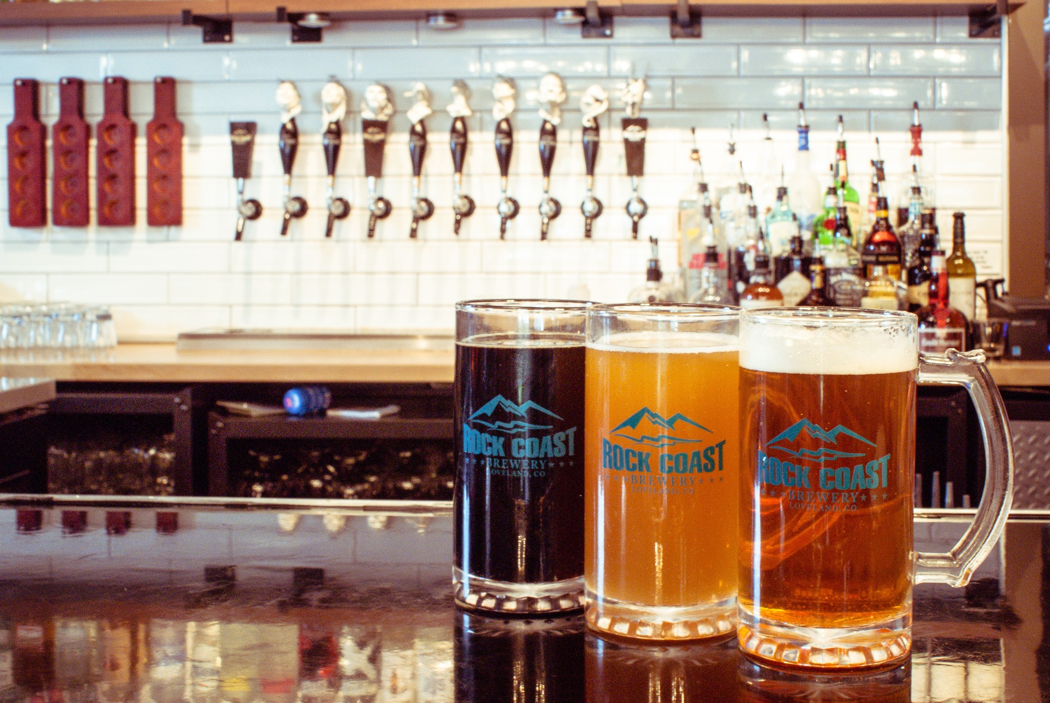 3 mugs of beer on the counter in front of taps