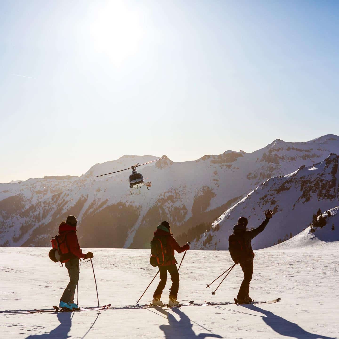 Tiga pemain ski di gunung dengan helikopter di belakang