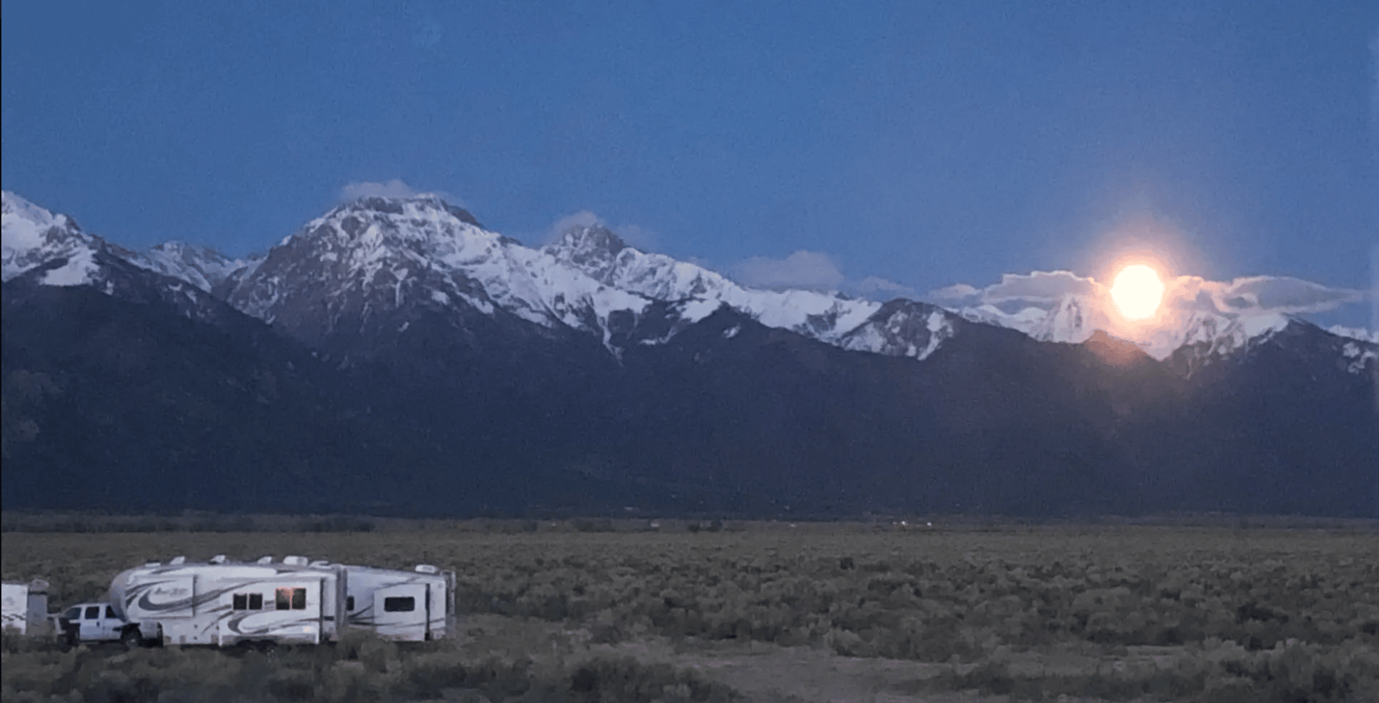 Moonlight over mountains and campers in a field