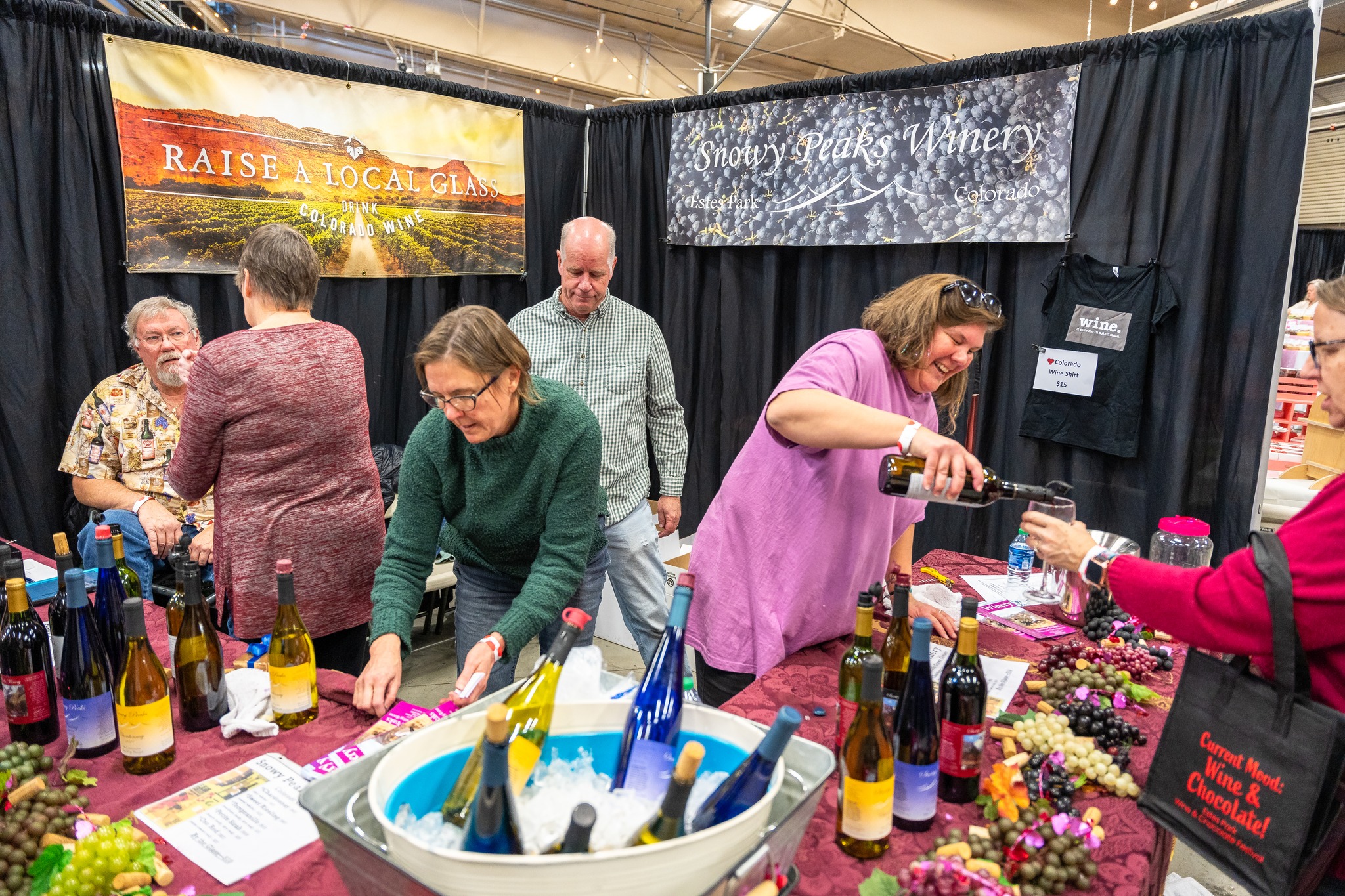 Several people behind a booth at the Estes Park Wine and Chocolate Festival pouring wine samples into guests glasses