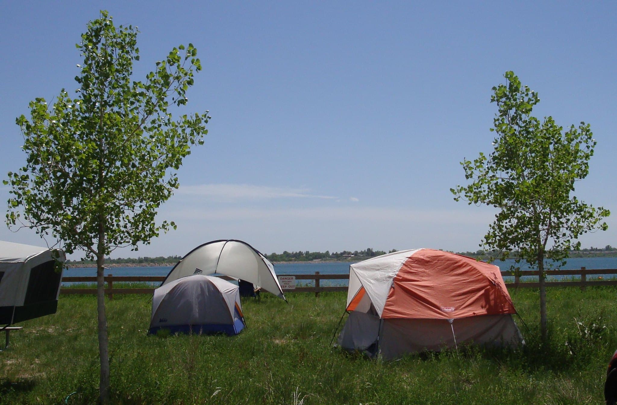 3 camping tents in the grass next to a lake