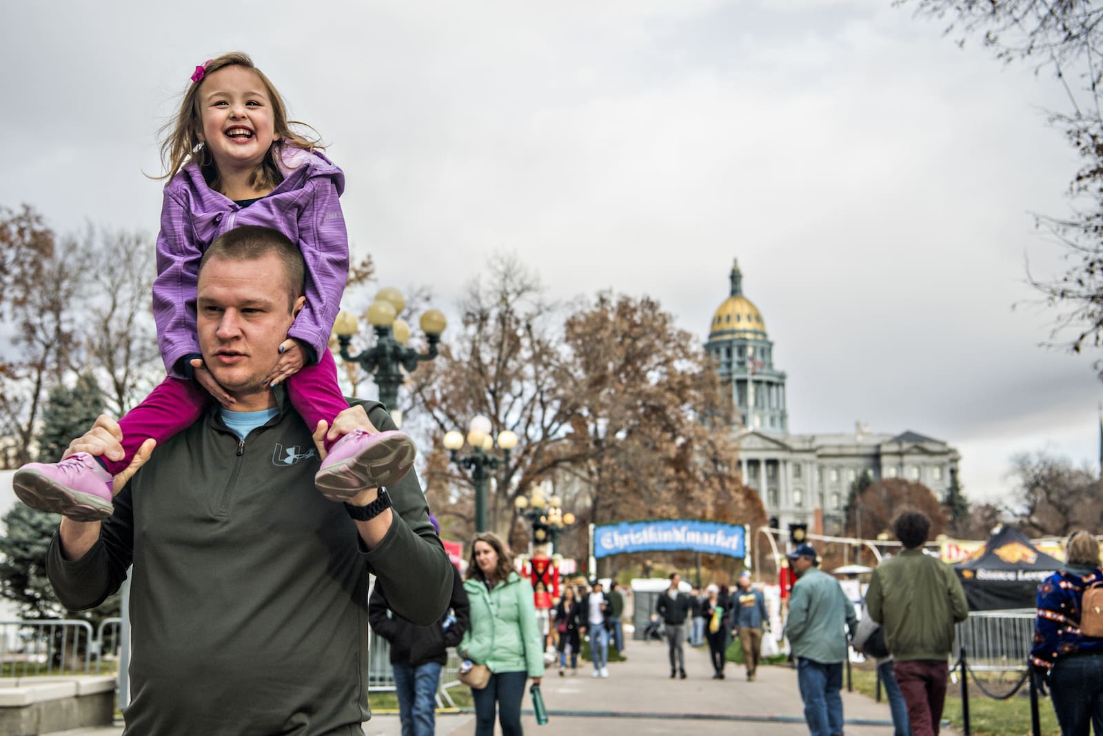 Denver Christkindlmarket a father walks with daughter on his shoulder