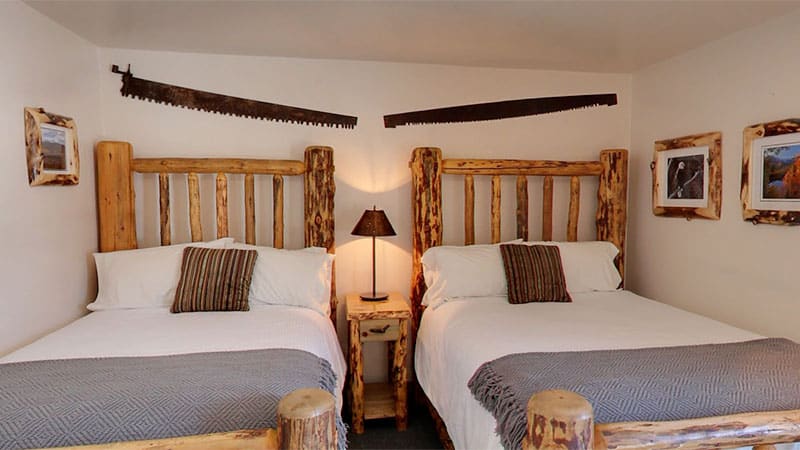 Two wooden framed hotel beds with white bedding and antique saw blades hanging above.