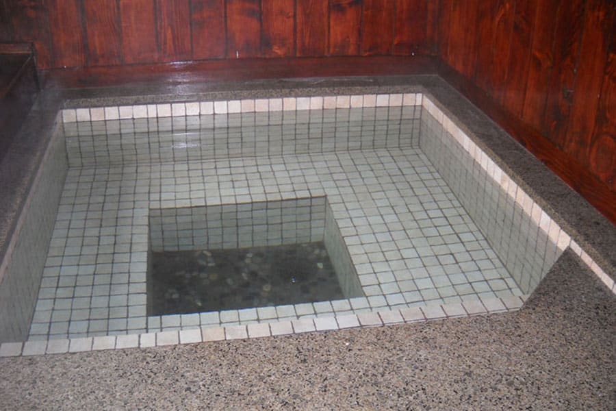 Square indoor soaking tub with white tiled seating around the edge. Wood paneling encloses the area