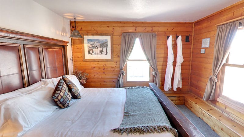 Large wooden paneled hotel room with a king bed and windows with natural light coming through