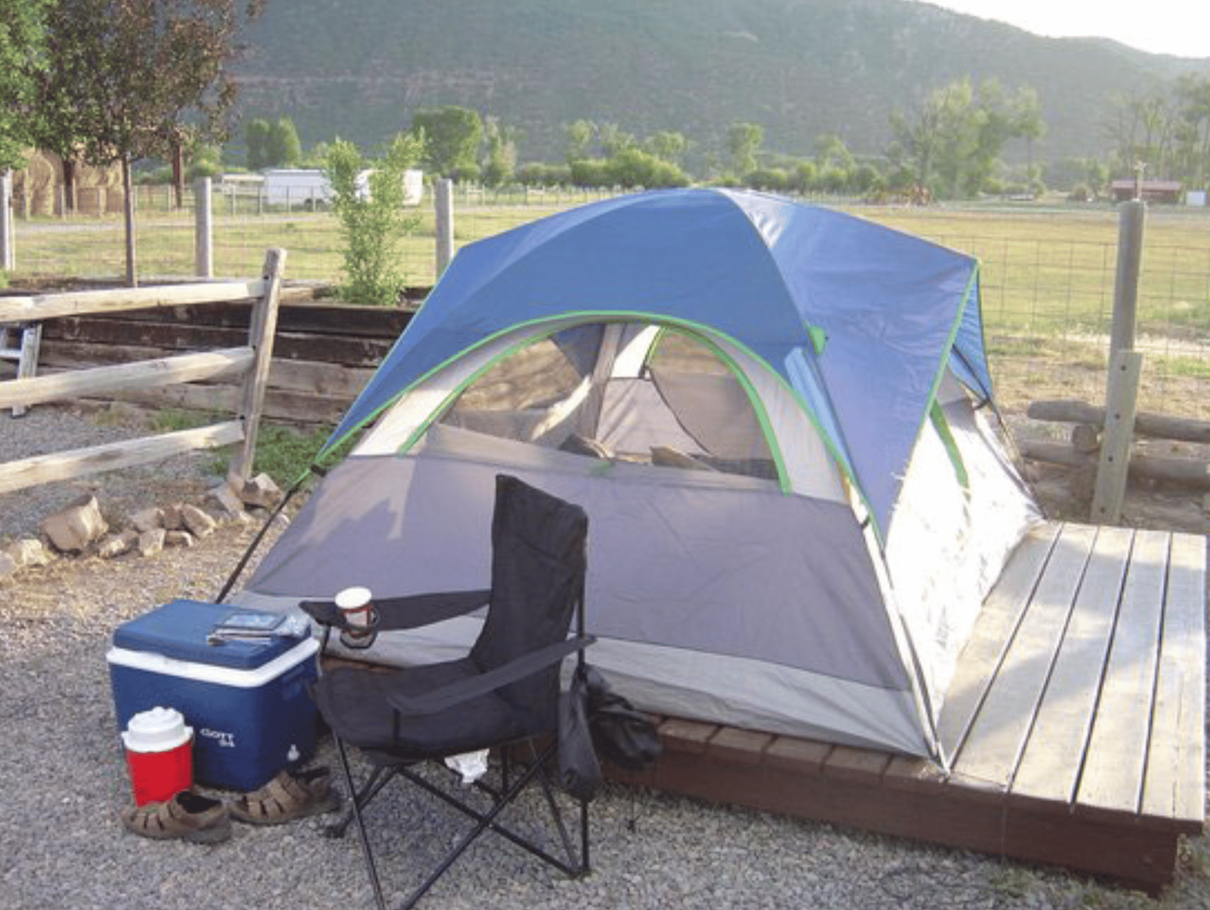 Blue tent pitched on a wooden tent pad with a camping chair and cooler in front