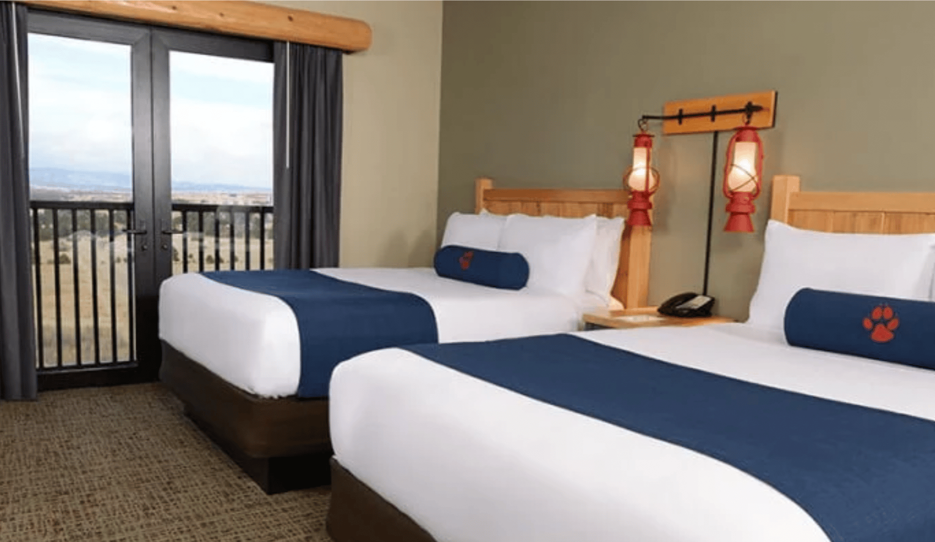 Two queen beds with blue and white linens and a balcony in a hotel room