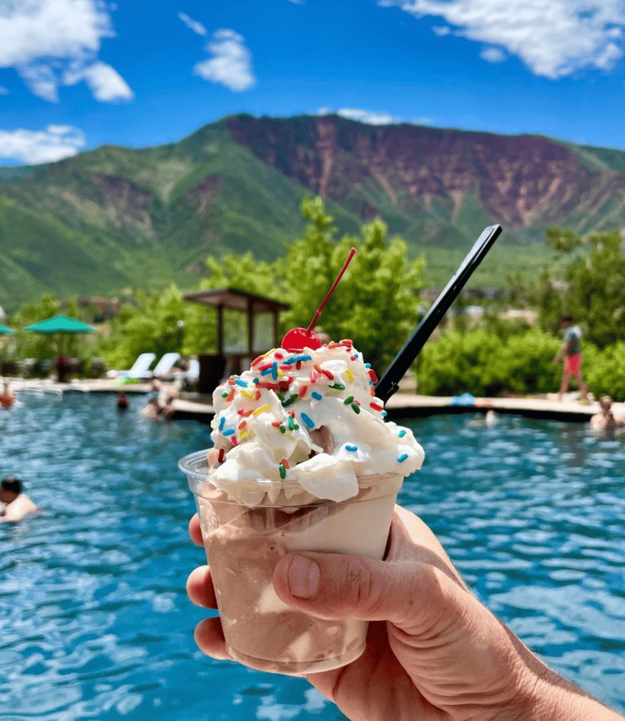 Holding a soft serve ice cream sundae in front of the hot springs pools