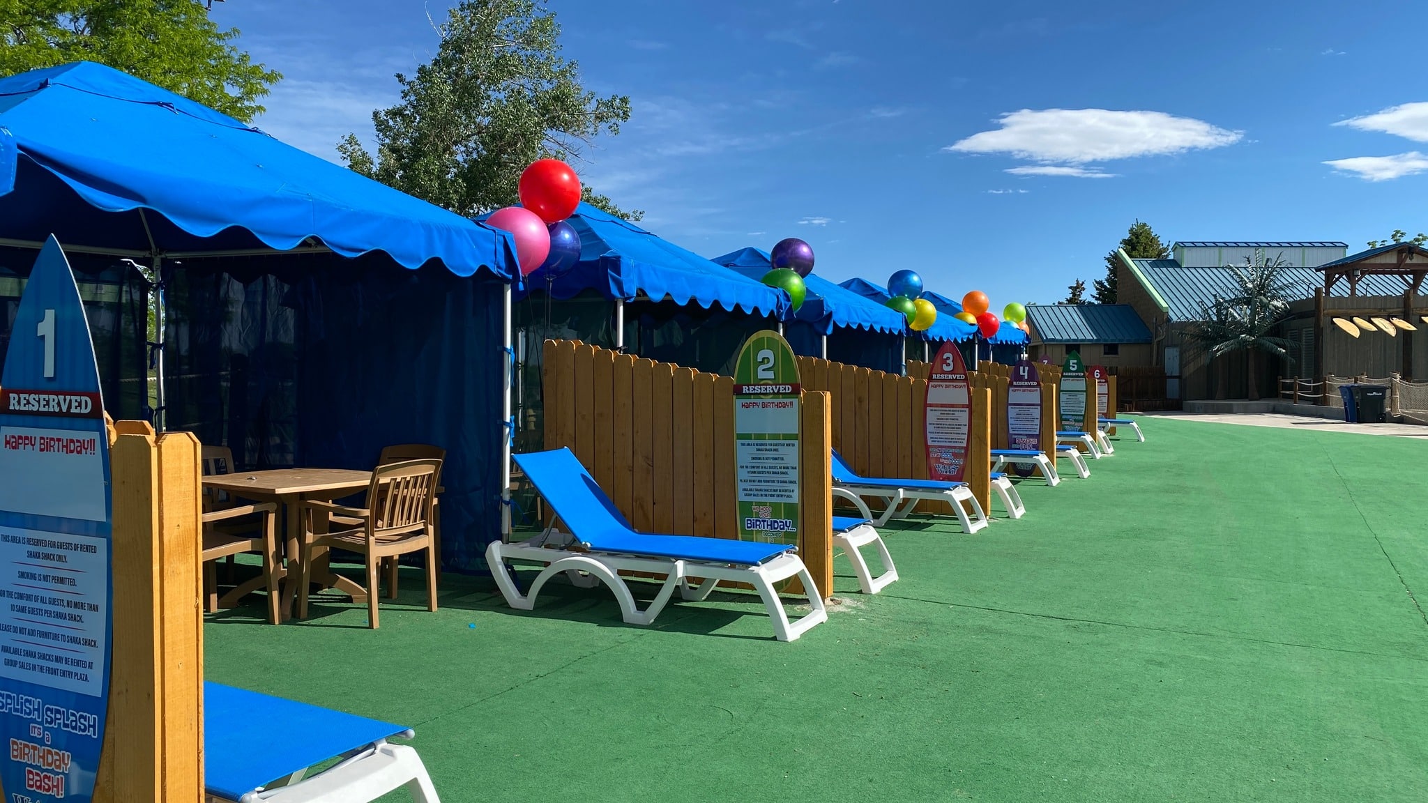 row of private cabanas at Water World. Blue square tents with blue sun lounge chairs on green turf