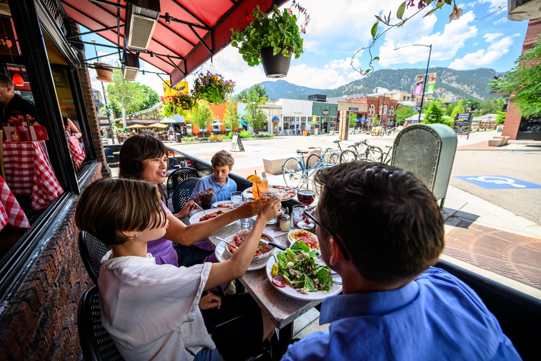 3 people sitting on the outdoor patio of a restaurant with a full table of food in front of them