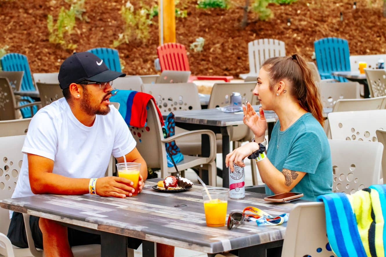 Two people sitting at a table at Water World drinking orange drinks and sharing a funnel cake