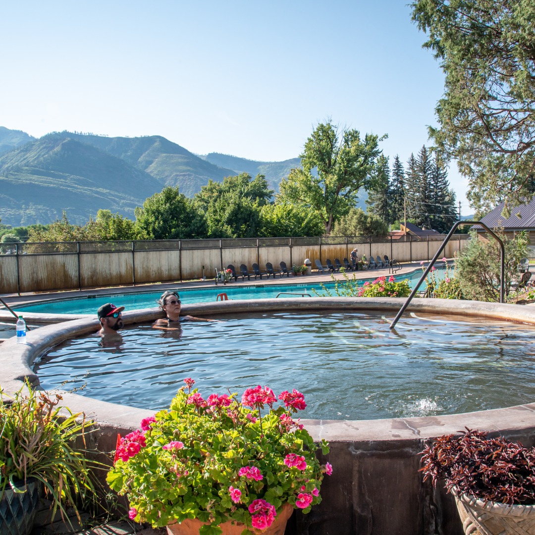 Stone hot springs pool with two people soaking in it on a sunny day