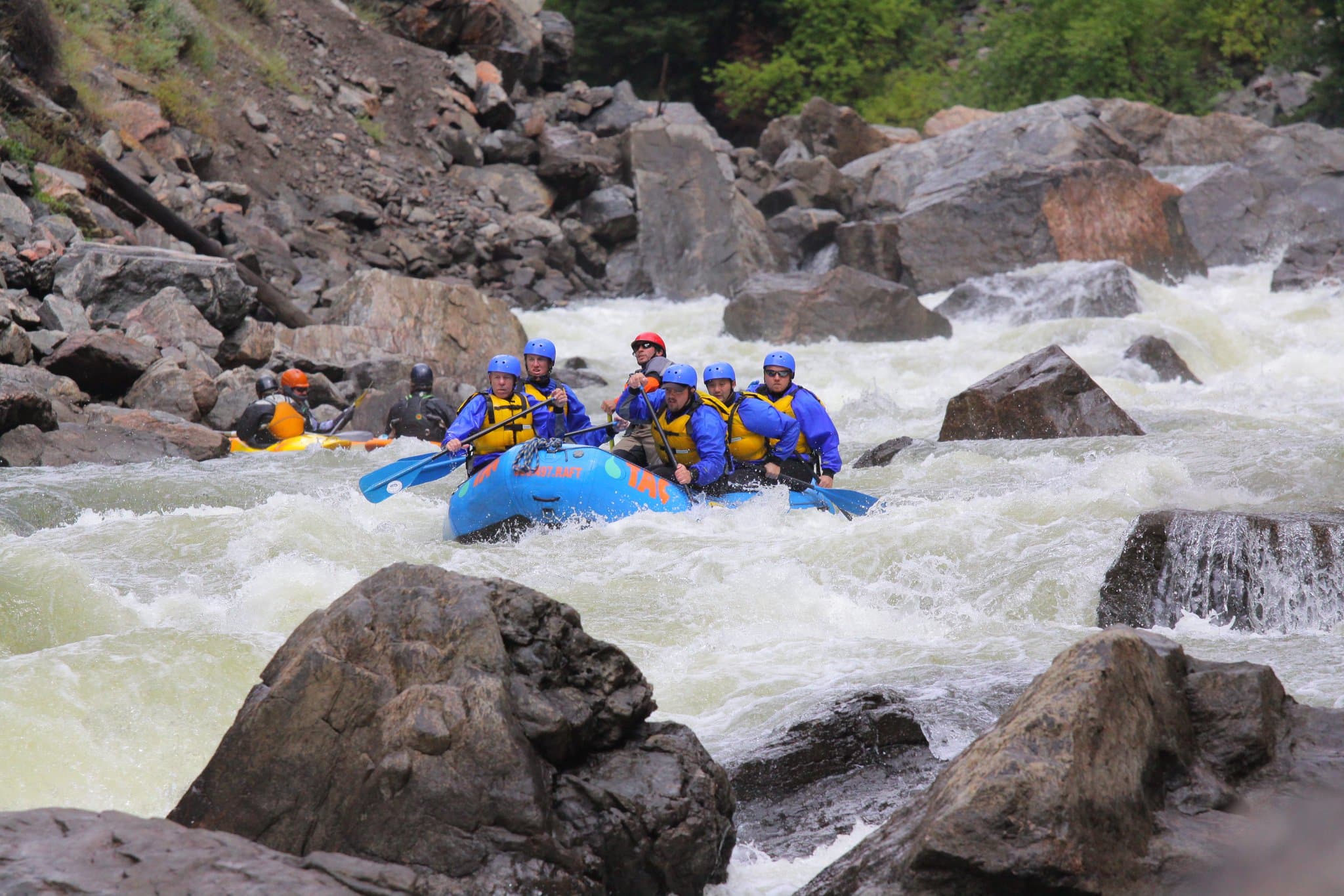 Group in life vests and helmets in a blue raft making their way through whitewater in Gore Canyon