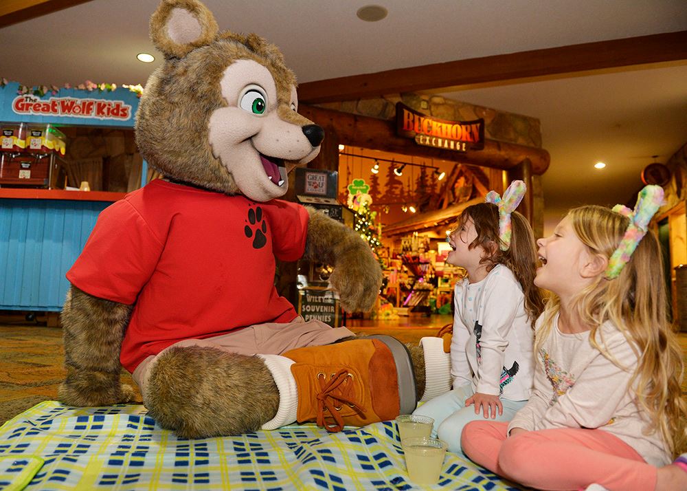 Person in a bear character costume sitting on the ground with two children