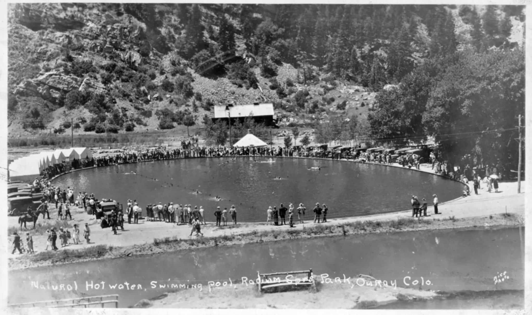 Black and white photo of historic hot spring pool with visitors gathered around the edges.