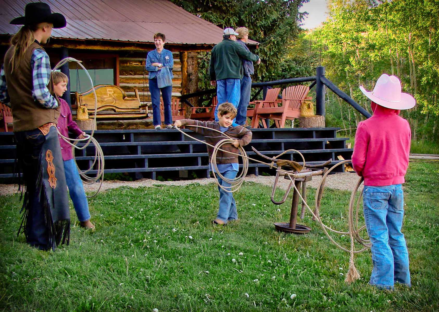 Group of children on the lawn at Latigo Ranch throwing lasso ropes onto a fake bull head