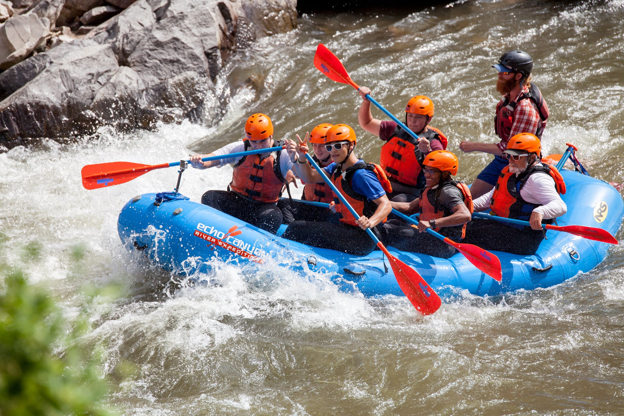 Several people in a blue whitewater raft using red paddles to whitewater raft in the Royal Gorge.