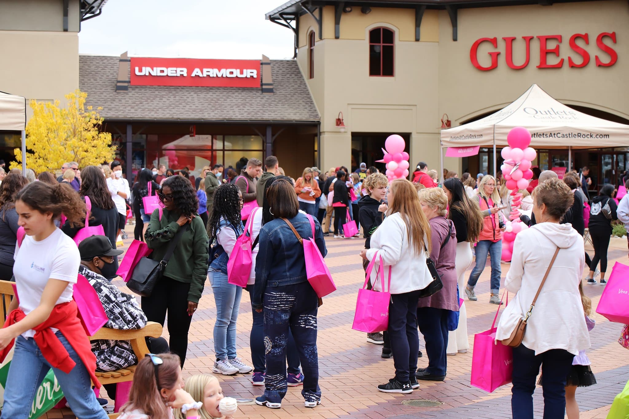 Dozens of shoppers standing in a plaza with pink reusable bags