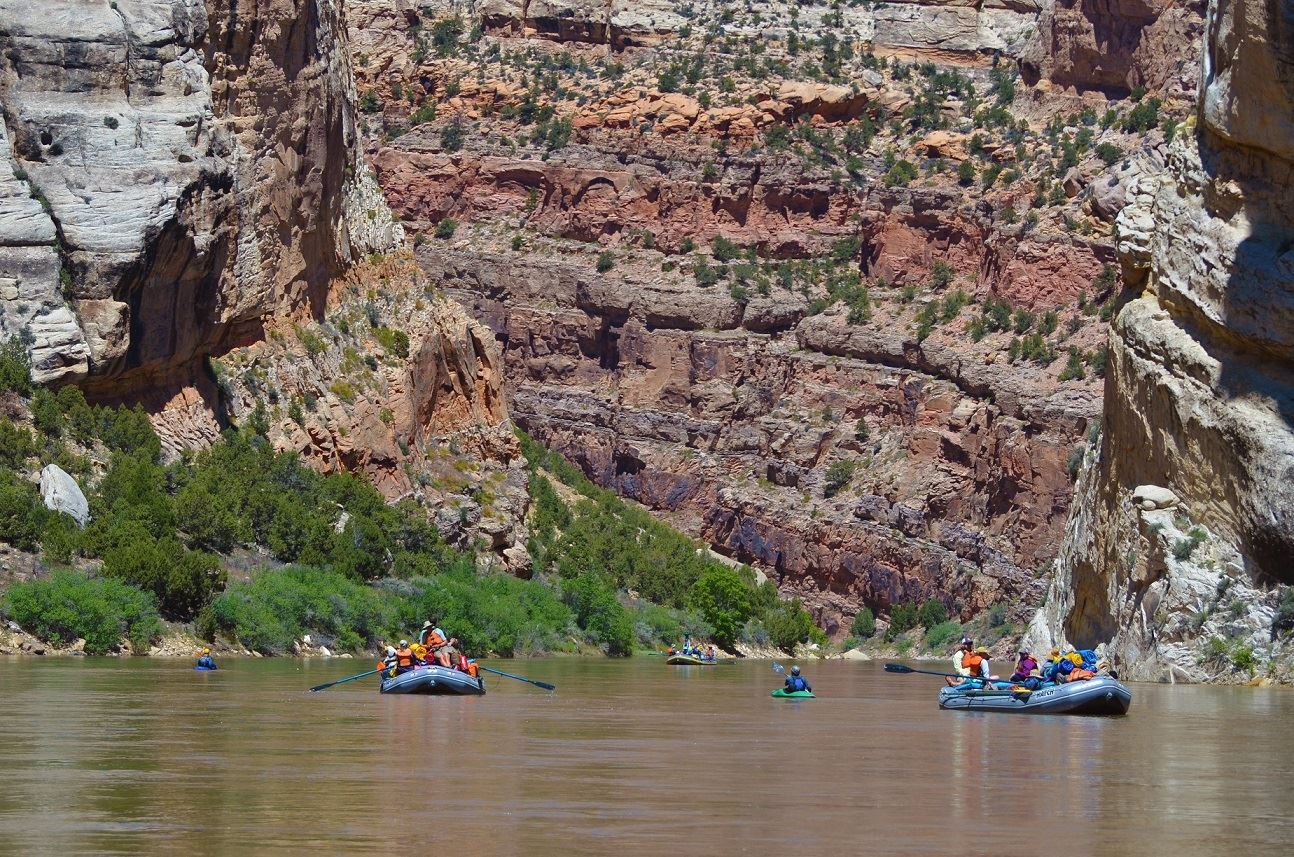 Massive layered red rock walls towering over rafters on the Yampa River