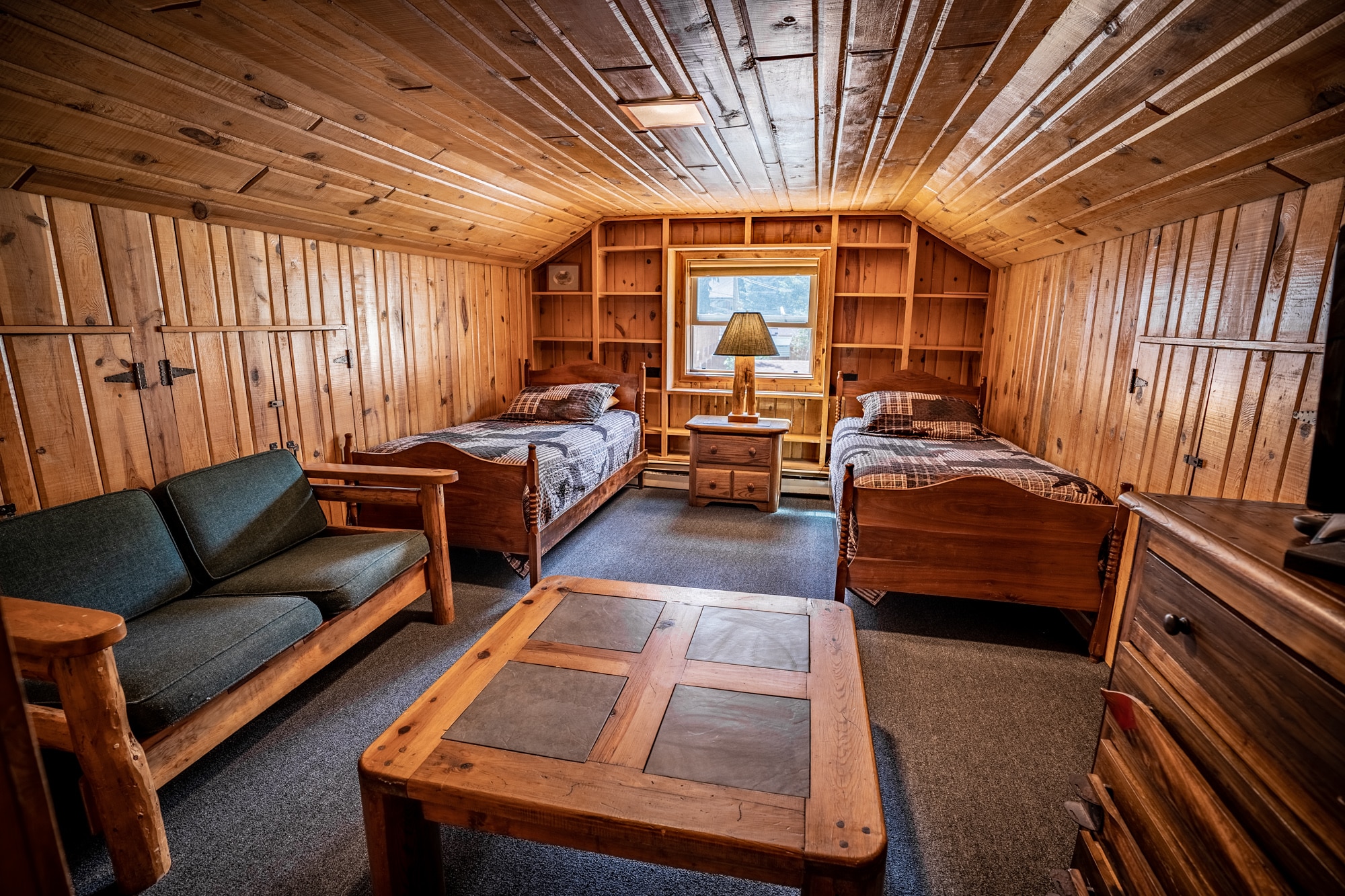 Inside of a log cabin with two twin beds, a couch, a coffee table and a dresser