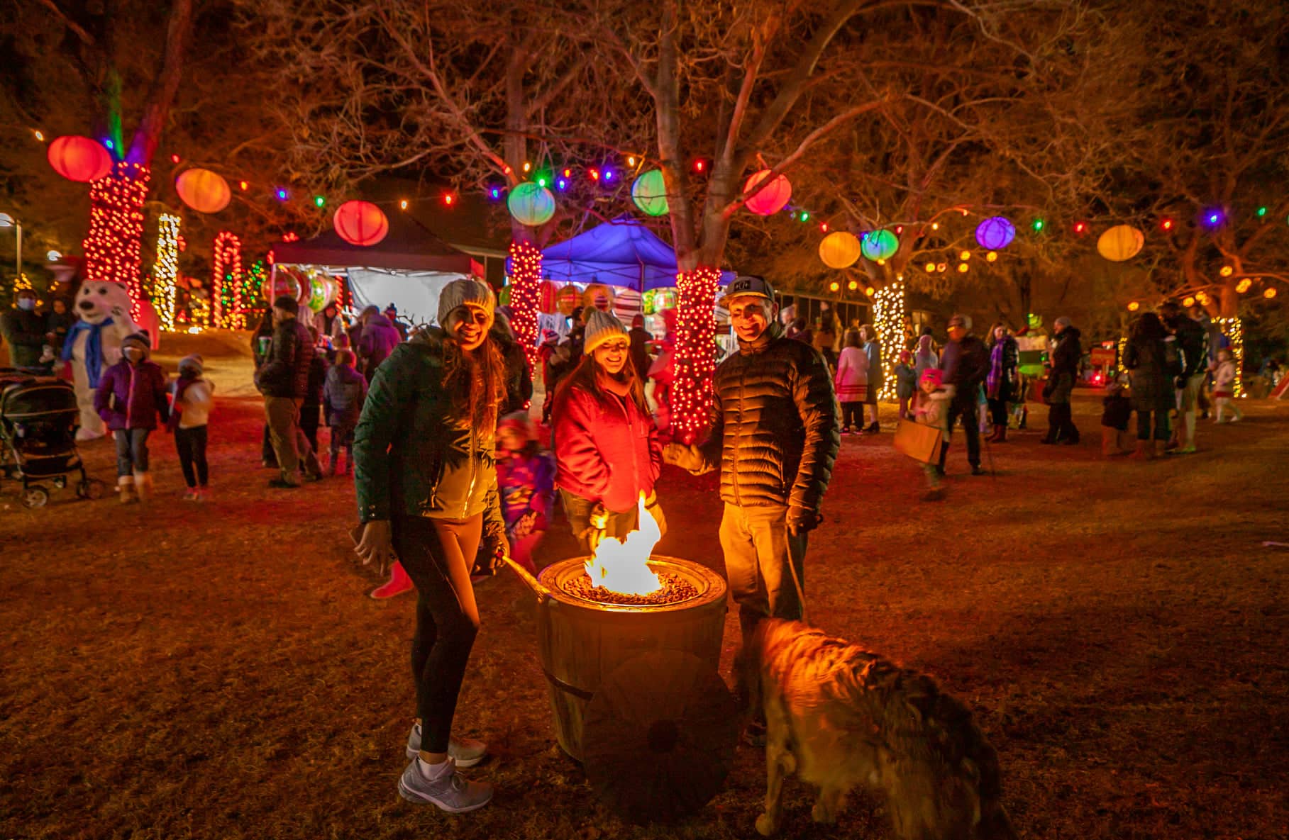 Three people gathered around a small fire pit at a holiday festival