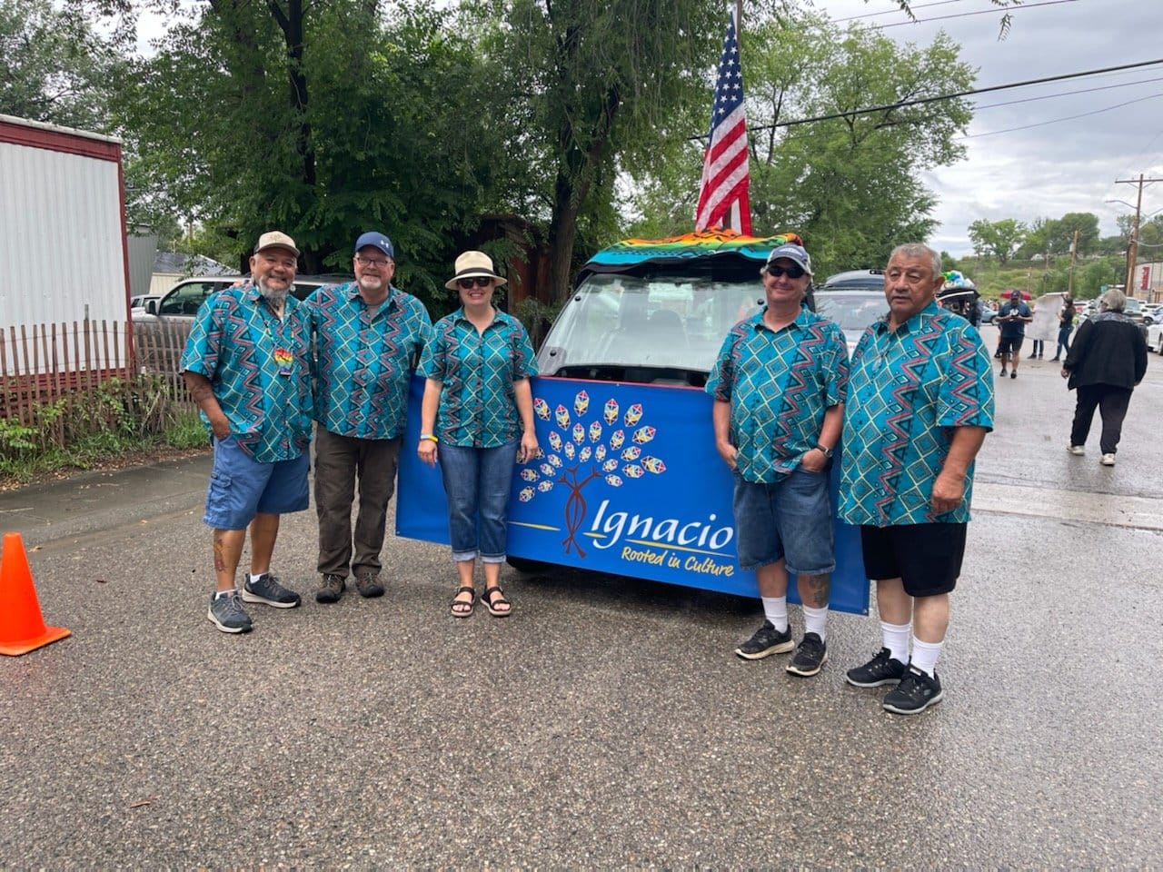 Four government board members standing in matching shirts next to a small parade float