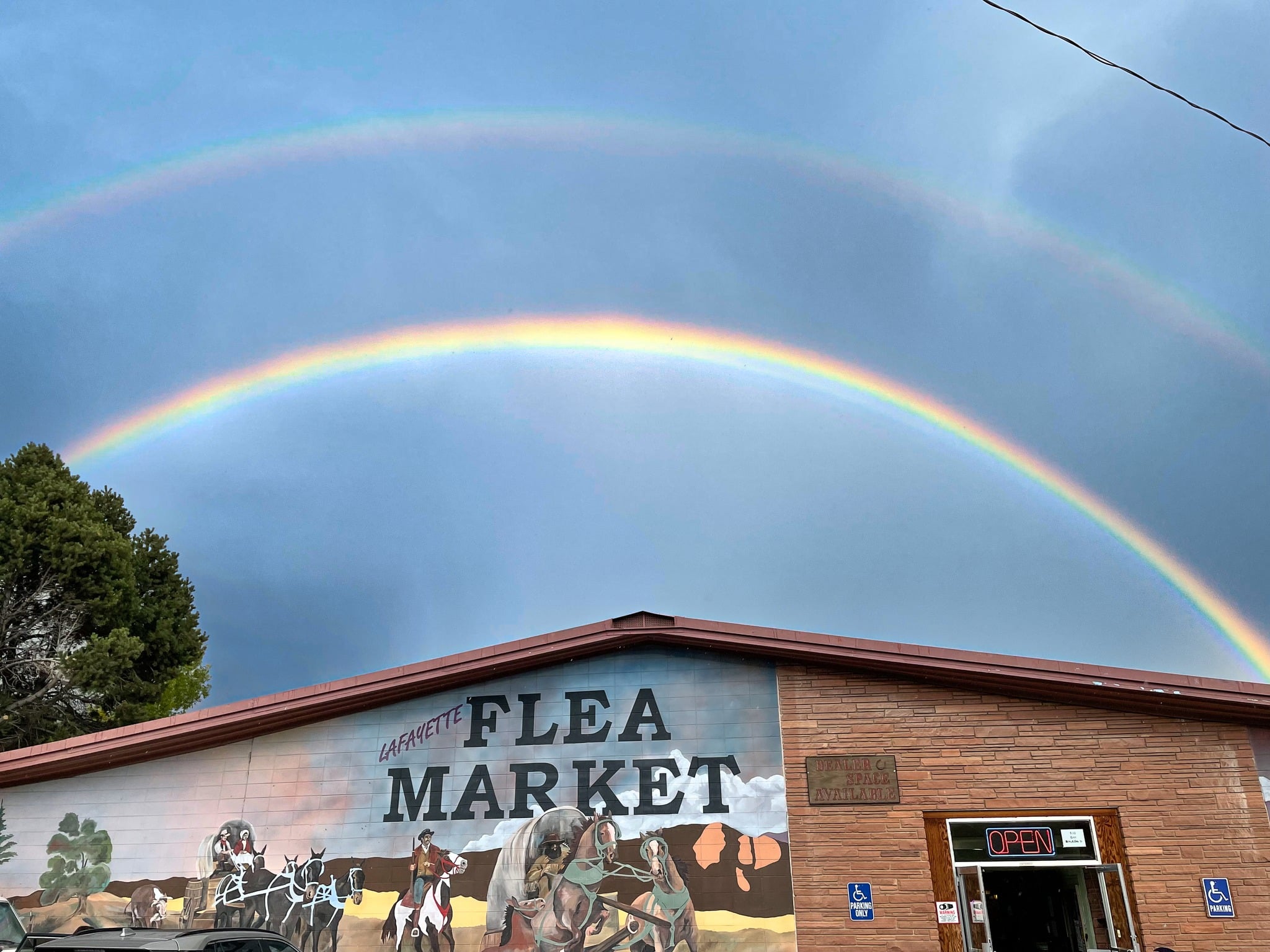 Double rainbow in the sky over a brick building painted with a mural for the Lafayette Flea