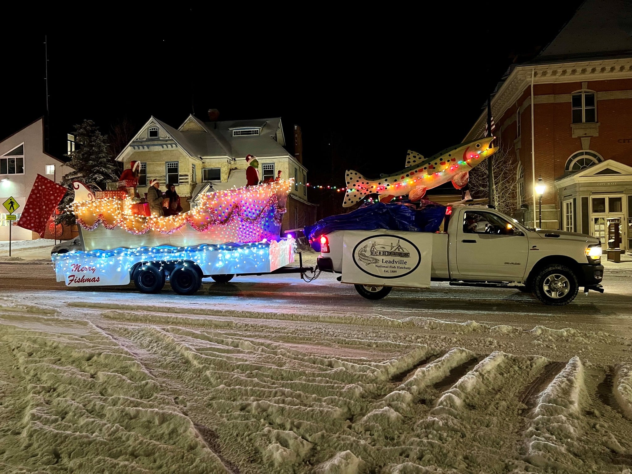 Parade float with white pickup truck pulling lit-up boat