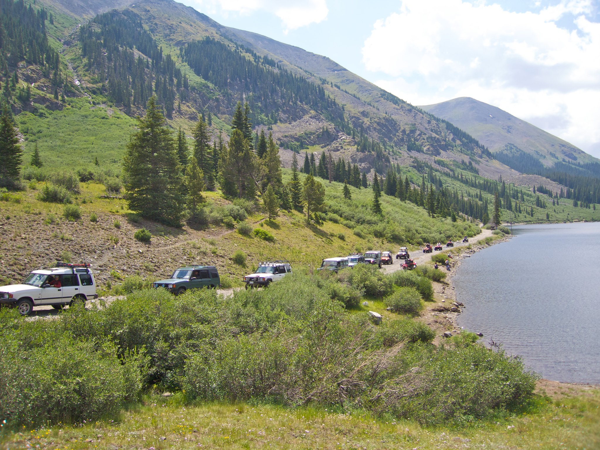 Line of cars on a dirt road by a lake