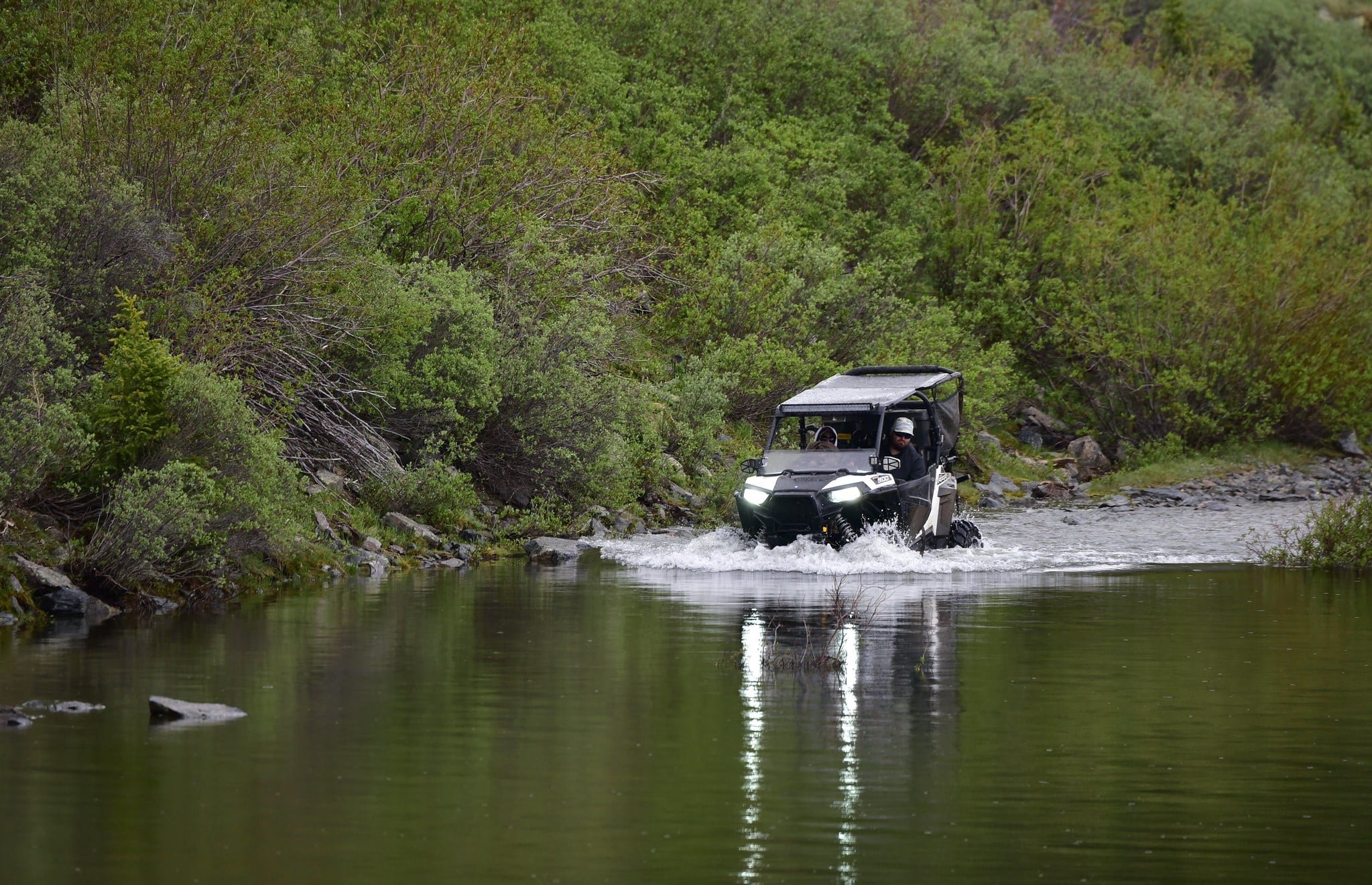 Off roading vehicle dipping into a lake surrounded by forest