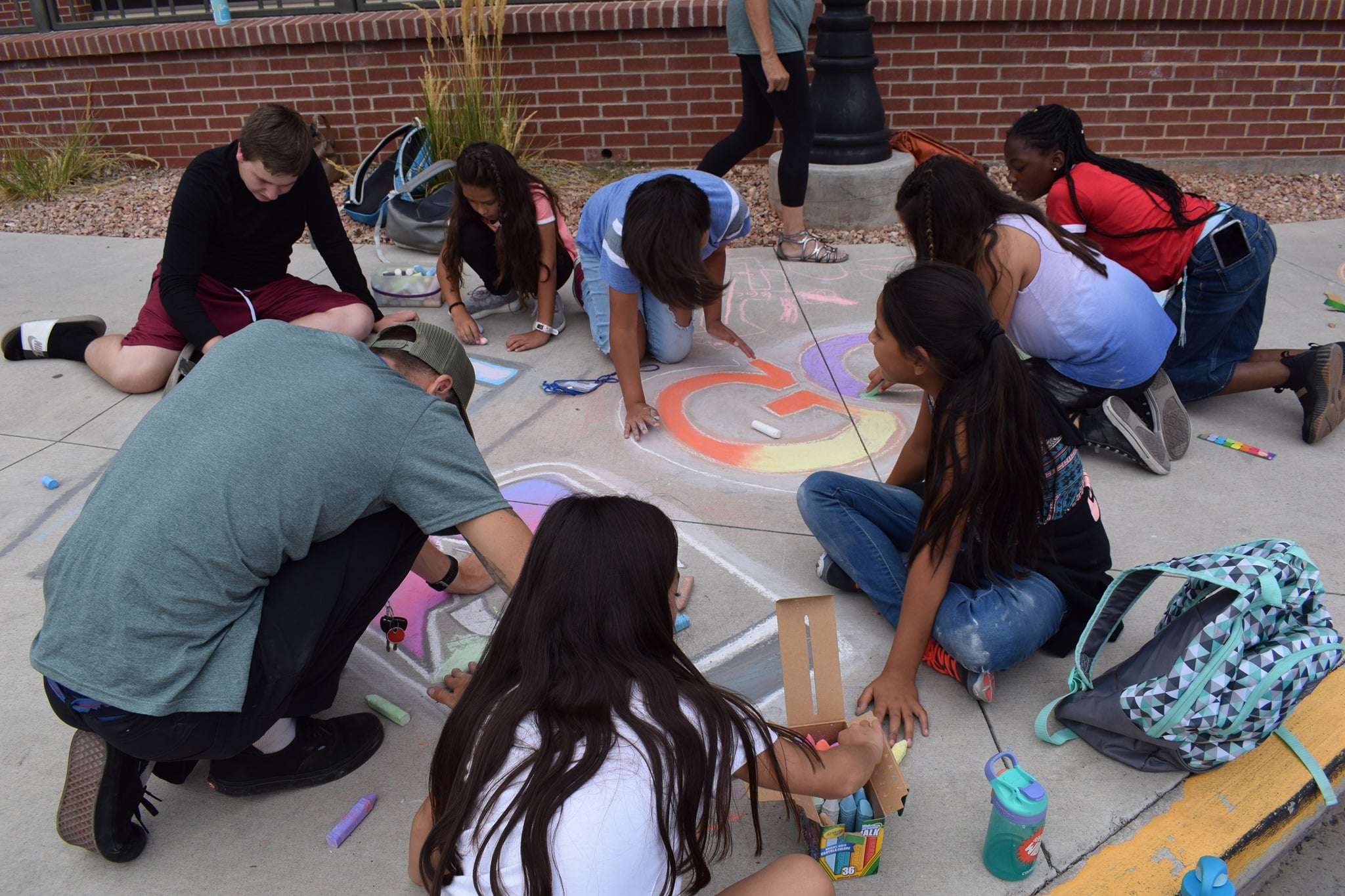 Group of children in a circle on a large sidewalk learning how to create chalk art at the Alamsa ARTsFestival