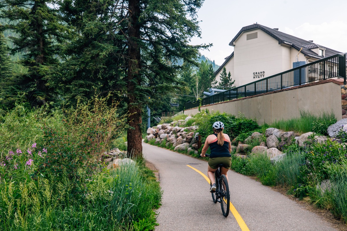 Woman biking on a path beside the Grand Hyatt Vail, Colorado