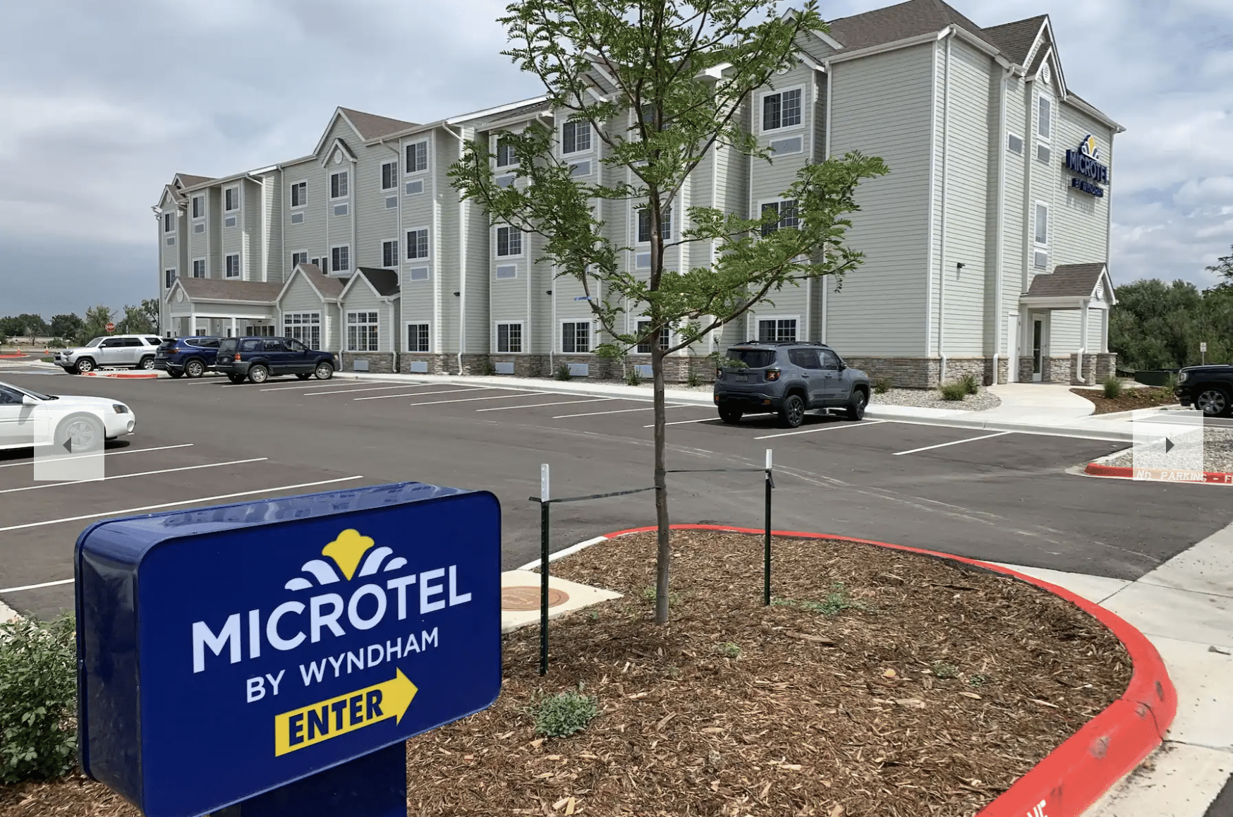 Blue entrance sign to Microtel hotel leading to a parking lot and two story hotel building