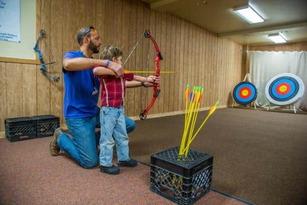 Man instructs boy how in archery inside Snow Mountain Ranch- YMCA of the Rockies