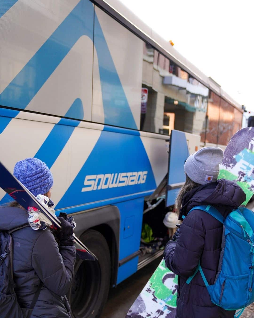 A woman skier and woman snowboarder board the Snowstang bus Colorado